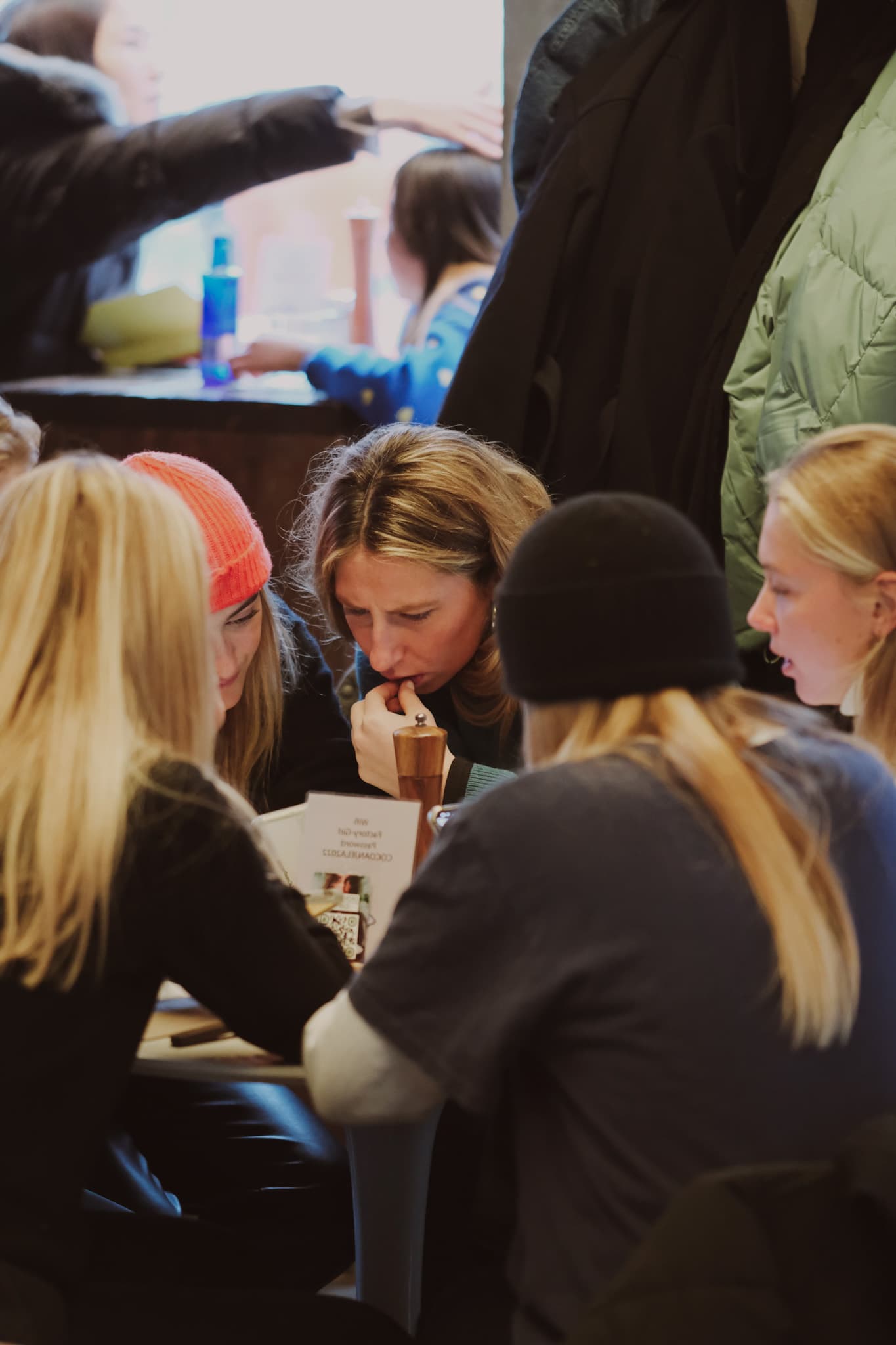 Friends leaning over a table during a lively daytime gathering at Factory Girl